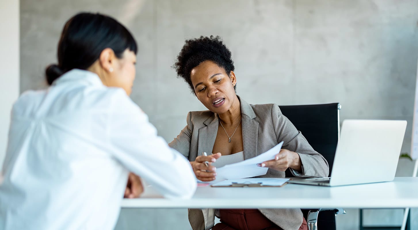 Two women seated at a table, reviewing papers and discussing data-driven insights for analytics in a collaborative setting.